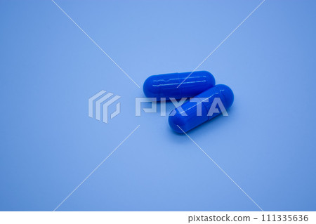 Two blue pills on blue background. Focus on foreground, shallow DOF. Close-up. Theme is treatment of diseases, medicine and pharmaceuticals. 111335636