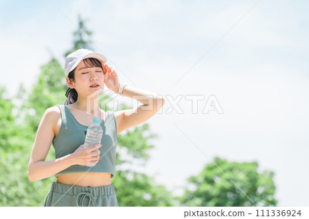 A woman who gets tired from training in the park (sweating, heat stroke, sunstroke, overheating) 111336924