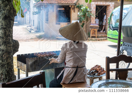 A woman grilling yakitori in front of a restaurant in Dong Lam village, designated as a national cultural property in Hanoi, Vietnam A woman grilling yakitori in front of a restaurant in Dong Lam village, designated as a national cultural property in Hanoi, Vietnam 111338666