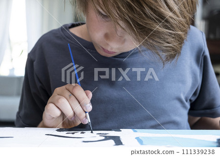 A boy, with long dark hair, draws a picture by numbers. 111339238