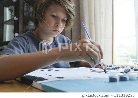 A boy, with long dark hair, draws a picture by numbers. 111339253