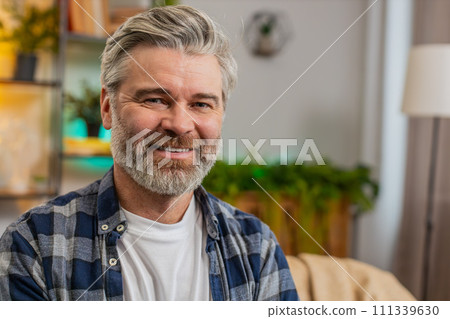 Happy smiling Caucasian senior middle-aged man sitting on sofa looking at camera and smiling at home 111339630