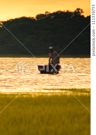 Silhouette of a man standing in the water next to his boat. 111339755