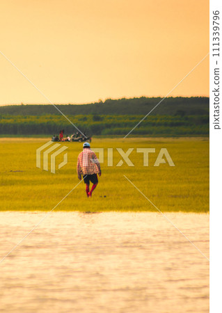 A farmer is walking in the fields. An old man is walking in the swamp. 111339796