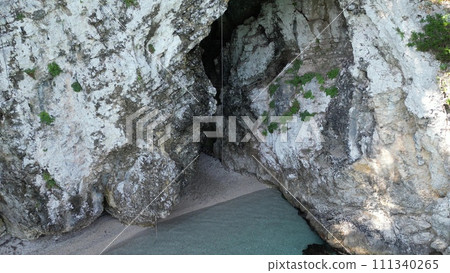 Greece, Corfu, Summer 2023. Beach Rovinia, Just a stunning beach in Rovinia with a small cave, with crystal clear waters and endless blue skies. Many boats with tourists, and children jumping from a c 111340265