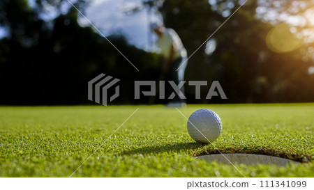 Golfer putting ball on the green golf, lens flare on sun set evening time. 111341099
