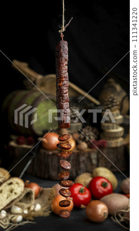 Smoked, aged sausage hanging in the kitchen with fresh vegetables and food ingrediets in the background Smoked, aged sausage hanging in the kitchen with fresh vegetables and food ingrediets in the background 111341220