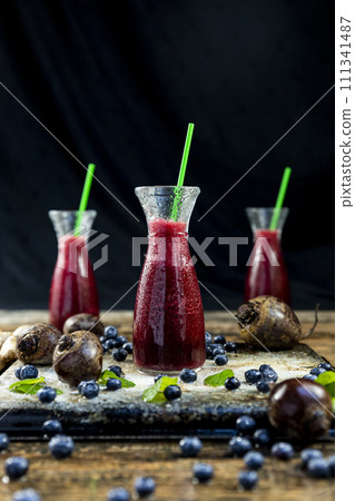 Juice with Beetroot, blueberries and mint in glass jar with fruits and vegetables on the wooden table. Detox, diet, healthy, vegetarian drink concept Juice with Beetroot, blueberries and mint in glass jar with fruits and vegetables on the wooden table. Detox, diet, healthy, vegetarian drink concept 111341487