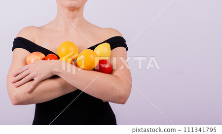 A female holding apples, lemons, oranges in different arms isolated on grey background. 111341795