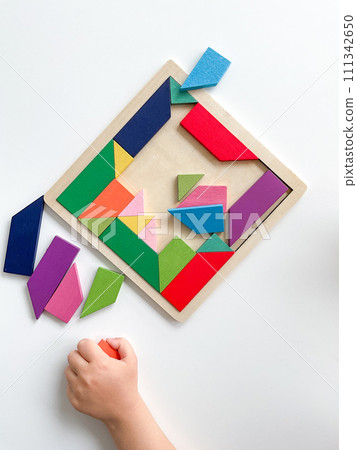 childs hand collects multicolored wooden mosaic on white background. 111342650