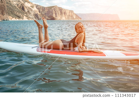 Woman sup sea. Sports girl on a surfboard in the sea on a sunny summer day. In a black bathing suit, he sits on a sapa in the sea. Rest on the sea. 111343017