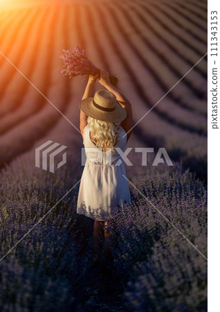 Blonde woman poses in lavender field at sunset. Happy woman in white dress holds lavender bouquet. Aromatherapy concept, lavender oil, photo session in lavender 111343153