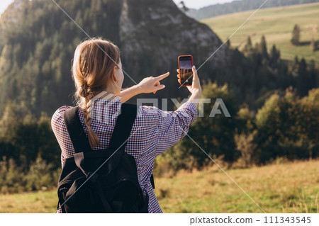 Tourist on top of the mountain takes a photo. Woman traveler takes a photo on a modern smartphone, makes beautiful pictures of beautiful mountain landscapes. Active lifestyle concept, rear view 111343545