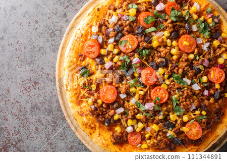Hot Tex Mex taco pizza with ground beef, salsa, cheddar cheese and Mexican spices close-up on a wooden board. Horizontal top view 111344891