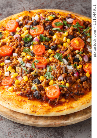Tex Mex taco pizza with ground beef, tomatoes, corn, black beans, cheddar cheese, red onion and Mexican spices close-up on a wooden board. Vertical 111344911