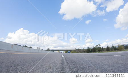 On a clear winter day, a car smoothly travels along Highway 101 near Santa Maria, California, under a brilliant blue sky, surrounded by a blend of greenery and golden hues. 111345131