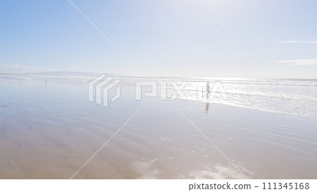 Little girl, braving the cold, joyfully runs in her swimsuit across the beach during winter. 111345168