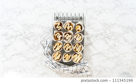 Flat lay. Garnishing no-yeast cinnamon roll cupcakes with cream cheese frosting from the piping bag. Flat lay. Garnishing no-yeast cinnamon roll cupcakes with cream cheese frosting from the piping bag. 111345199