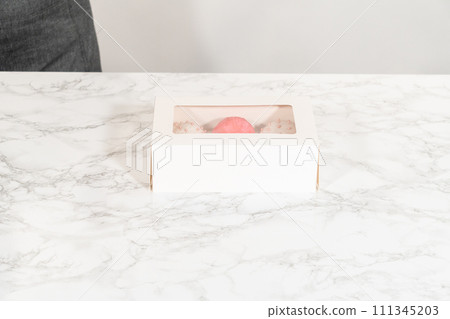 The birthday cupcakes, beautifully embellished with fondant decorations, are being carefully placed into white paper boxes, ready for their grand presentation. The birthday cupcakes, beautifully embellished with fondant decorations, are being carefully placed into white paper boxes, ready for their grand presentation. 111345203