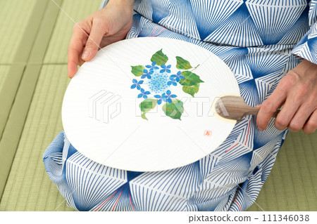 A middle-aged woman in a yukata sitting on a tatami mat in a Japanese-style room and holding a fan A middle-aged woman in a yukata sitting on a tatami mat in a Japanese-style room and holding a fan 111346038