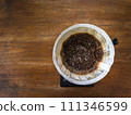 Coffee grounds after pouring water through the dripper with filter paper. On digital scale, placed on the wooden table. In top view. 111346599