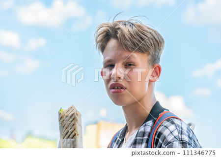 Blond teenager enjoying chicken shawarma in park on summer day 111346775
