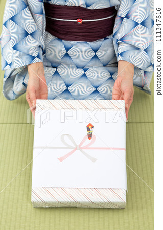 一位穿著浴衣的中年婦女坐在日式房間的榻榻米上，手裡拿著年中禮物 111347816