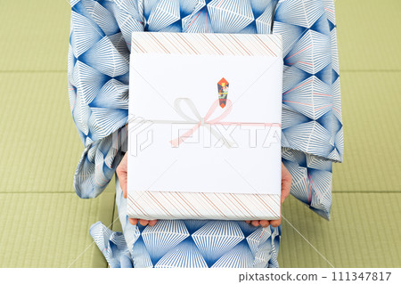 一位穿著浴衣的中年婦女坐在日式房間的榻榻米上，手裡拿著年中禮物 111347817