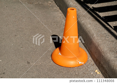 A traffic orange cone is used as a barrier during road construction work A traffic orange cone is used as a barrier during road construction work 111348008