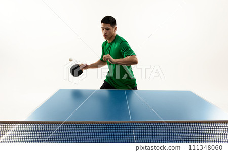 Focused table tennis serve from Asian player in vibrant green sportswear in motion against white studio background. Froze moment. 111348060
