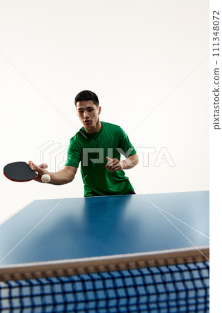 Asian sportsman playing table tennis, eyeing ball for precise hit and make goal in motion against white background. Asian sportsman playing table tennis, eyeing ball for precise hit and make goal in motion against white background. 111348072