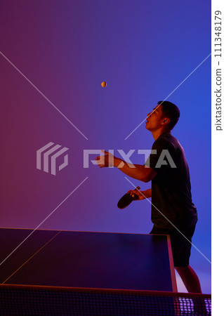 Young man, player ready to hit ball in neon-lit table tennis match against gradient pink-blue background. Dynamic gel portrait. Young man, player ready to hit ball in neon-lit table tennis match against gradient pink-blue background. Dynamic gel portrait. 111348179