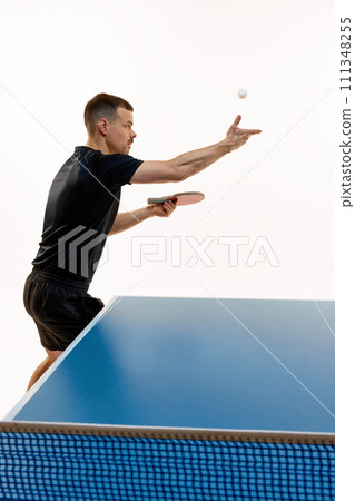 Side view portrait of young athlete man serving ball in table tennis keeping eyes on floating ball against white background. Copy space. Side view portrait of young athlete man serving ball in table tennis keeping eyes on floating ball against white background. Copy space. 111348255