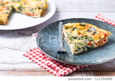 Italian Frittata made with spinach, tomatoes, onion and peppers on white wooden table 111350090