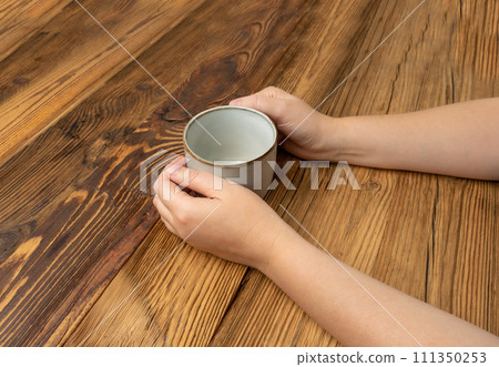 Hand Holds Cup, Empty Cup in Hands, Coffee Mug, Teacup Mockup, Cup in Arms on Wooden Table Hand Holds Cup, Empty Cup in Hands, Coffee Mug, Teacup Mockup, Cup in Arms on Wooden Table 111350253
