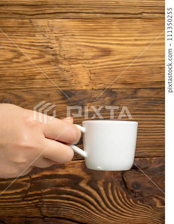 Hand Holds Cup, Empty White Cup in Hands, Coffee Mug, Teacup Mockup, Cup in Arms on Wooden Table 111350255