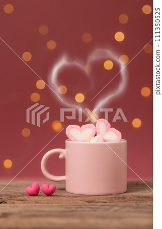hot drink with heart shape smoke on pink coffee cup with heart shape marshmallow on top, with two small heart placed side by side on wooden table, bokeh light at background. romantic love relationship hot drink with heart shape smoke on pink coffee cup with heart shape marshmallow on top, with two small heart placed side by side on wooden table, bokeh light at background. romantic love relationship 111350525