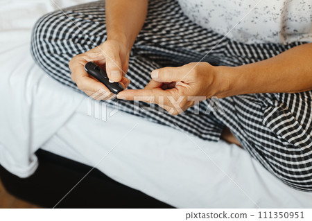 man pricks his finger to measure his glucose level 111350951
