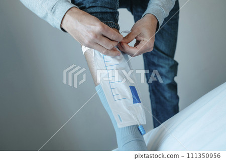 young man attaches his urine drainable leg bag 111350956