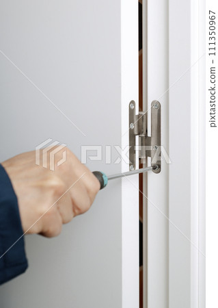man screwing or unscrewing the hinge of a door 111350967