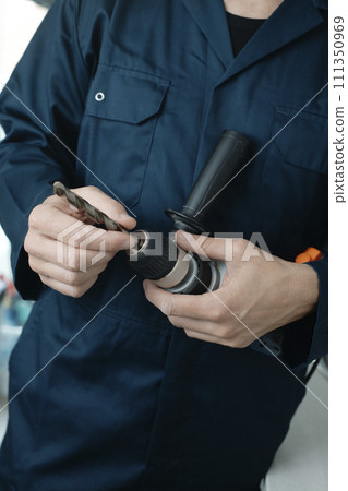 man puts a drill bit in an electric drill 111350969