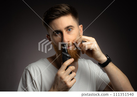 A young guy uses a nose trimmer to remove nose hair 111351540