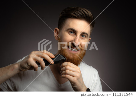 Handsome young bearded man trimming his beard with a trimmer 111351544