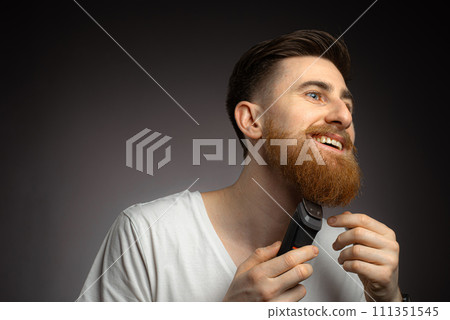 Handsome young bearded man trimming his beard with a trimmer 111351545