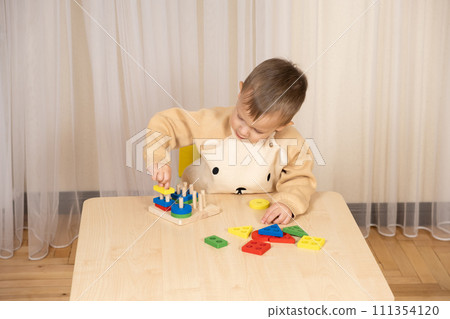 A two-year-old boy plays with wooden toys to develop logic and motor skills A two-year-old boy plays with wooden toys to develop logic and motor skills 111354120