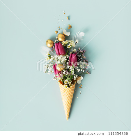 Ice cream cone with beautiful flowers and golden easter eggs on blue background flat lay 111354866