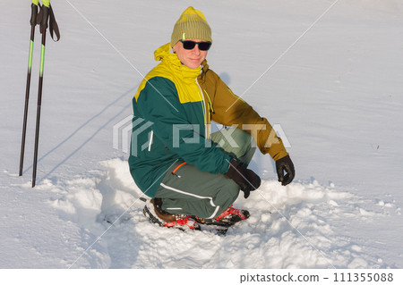 Man on meadow in winter with trekking poles and snowshoes, sunny morning after snow falling. 111355088