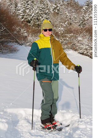 Man on meadow in winter with trekking poles and snowshoes, sunny morning after snow falling. Man on meadow in winter with trekking poles and snowshoes, sunny morning after snow falling. 111355090