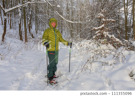 Man in forest in winter with trekking poles and snowshoes, sunny morning after snow falling. Man in forest in winter with trekking poles and snowshoes, sunny morning after snow falling. 111355096