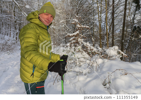 Man has dressed down jacket, in forest in winter with trekking poles and snowshoes, sunny morning after snow falling. Man has dressed down jacket, in forest in winter with trekking poles and snowshoes, sunny morning after snow falling. 111355149
